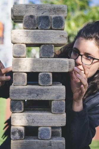 A person wearing glasses contemplates how they'll pull out the next wooden block in a game of Jenga. 